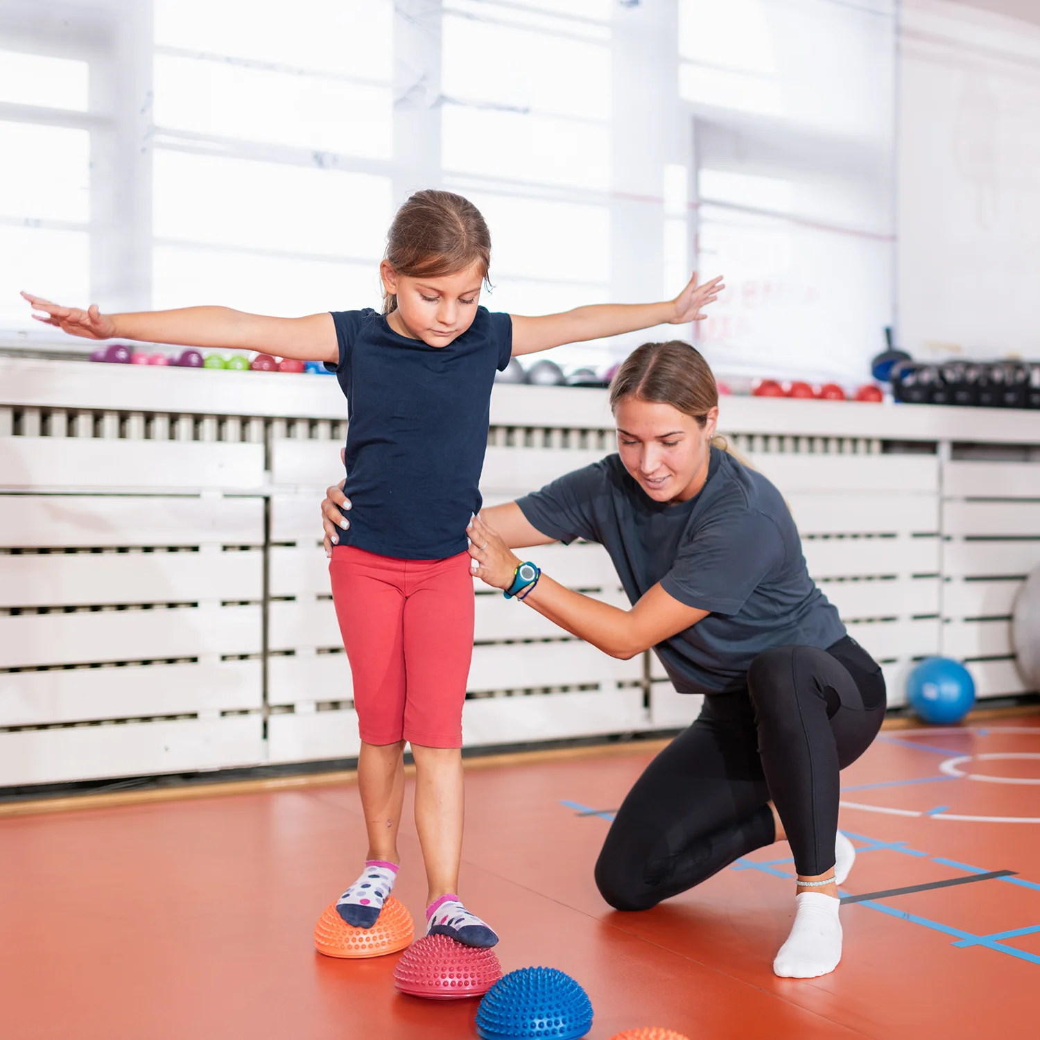 girl balancing with therapist in bright indoor gym