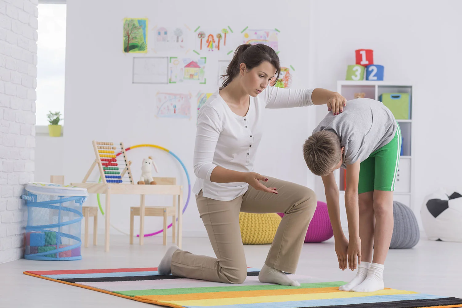 woman helping child stretch in playroom indoors